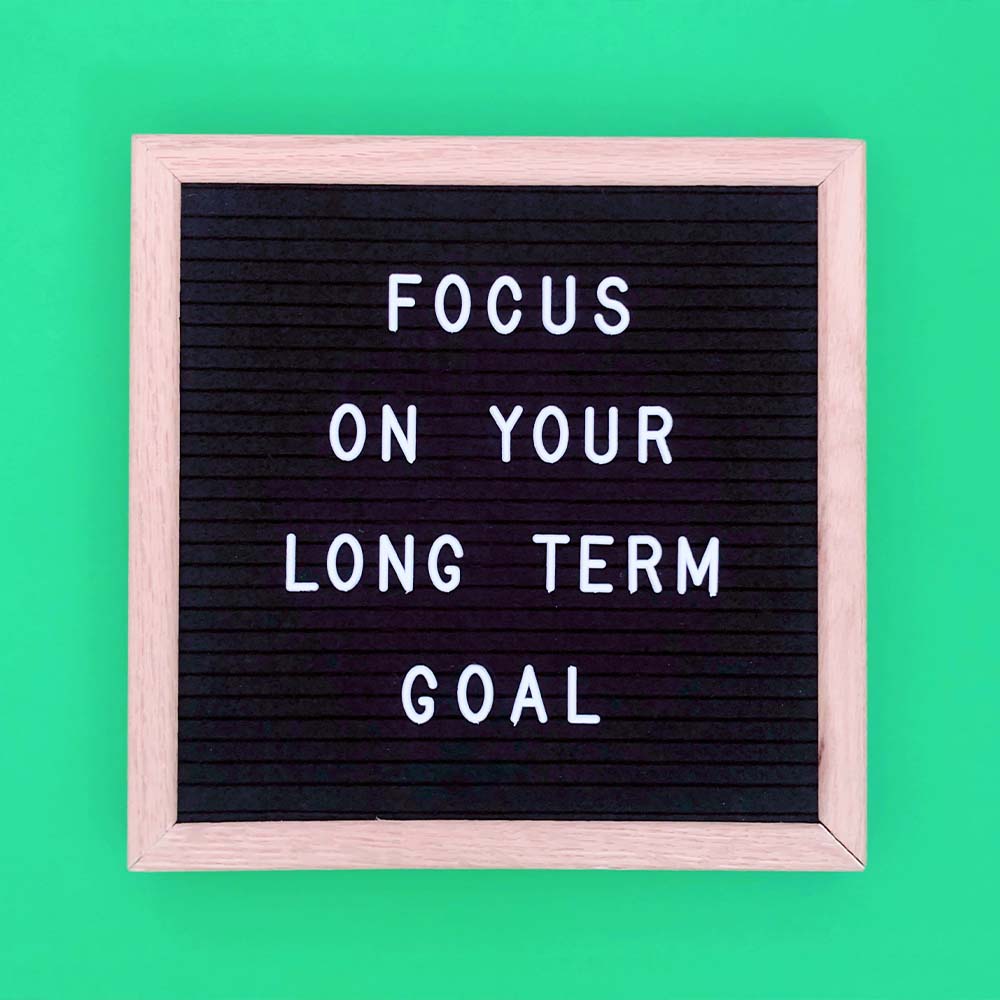 A black letter board with a wooden frame displaying the message, 'FOCUS ON YOUR LONG TERM GOAL' in white capital letters, set against a green background.